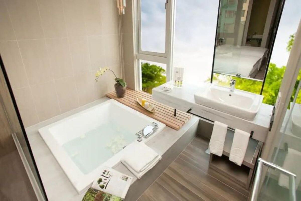 Un baño moderno con una bañera grande, un tocador con espejo y una ventana que ofrece vistas a zonas verdes.
