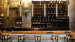 Uma área de bar com um balcão comprido, várias prateleiras com potes e algumas cadeiras.