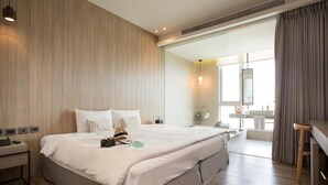 Quarto de hotel moderno com uma cama grande, mesas de cabeceira, uma escrivaninha e um banheiro visível através de uma porta aberta.