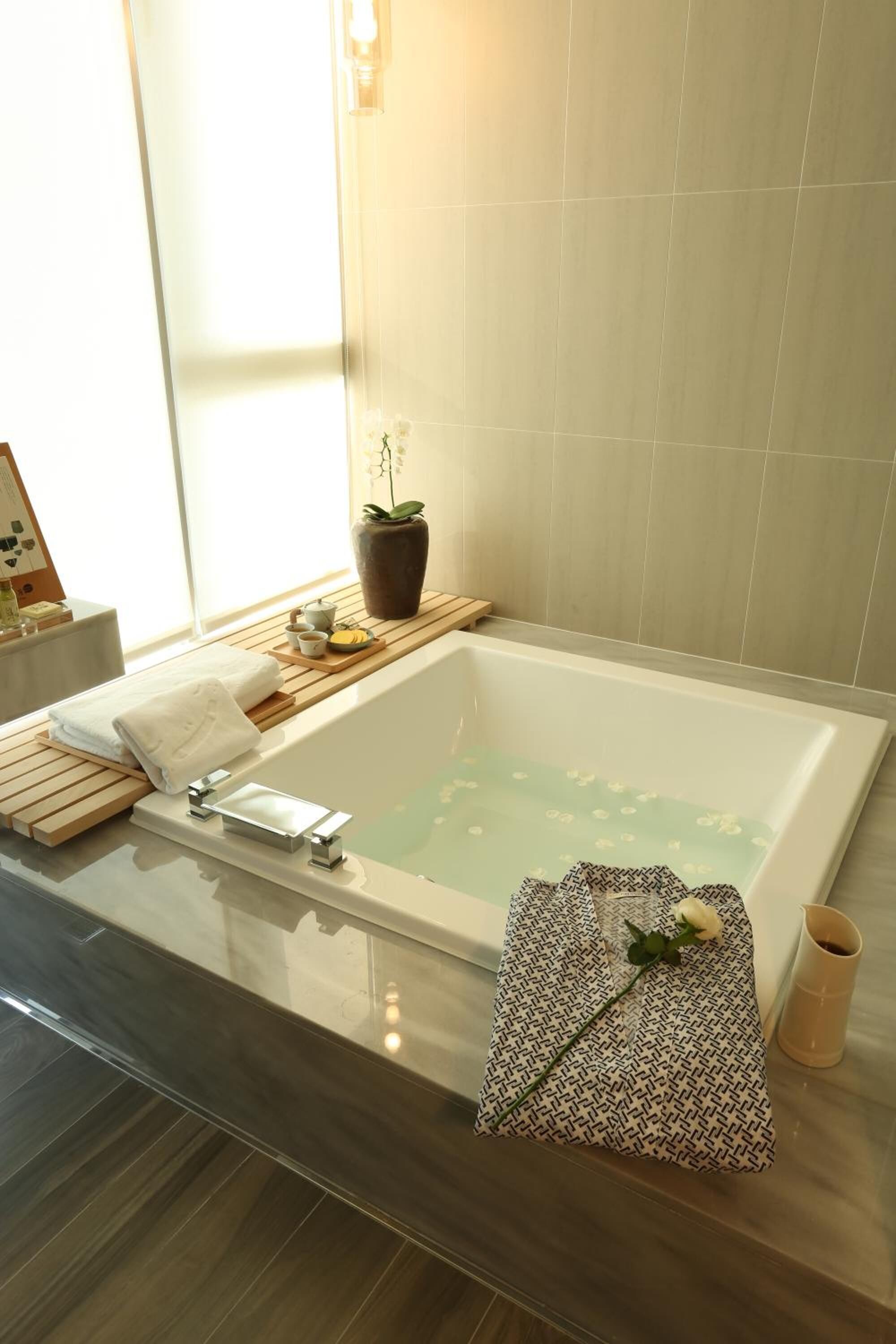 Un baño moderno con una bañera grande, una mesita de madera y una planta en maceta.
