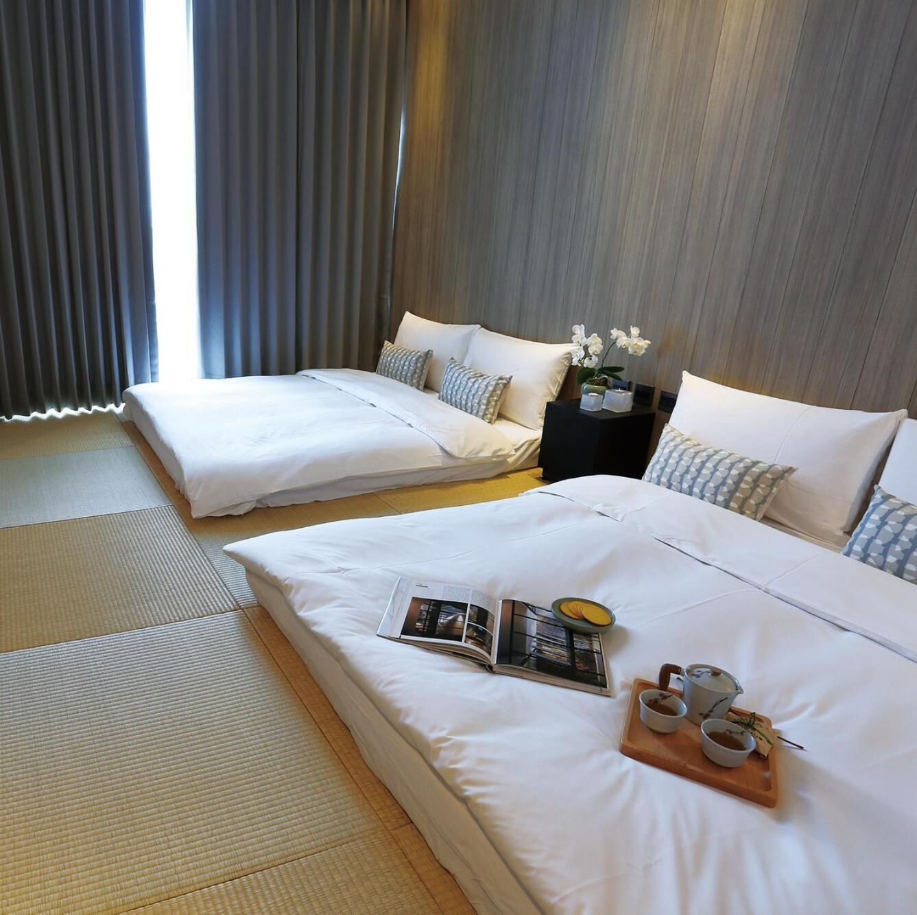 A hotel room with two beds, a nightstand, and a tray with tea and cups.
