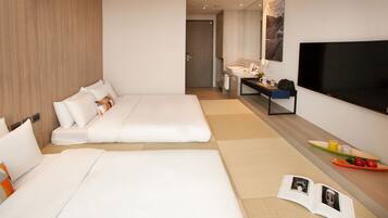 A hotel room with two beds, a bathroom, a TV, and a small table with a tray of fruit.
