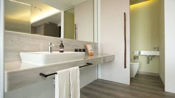 A modern bathroom with a large sink, mirror, and a toilet visible in the background.