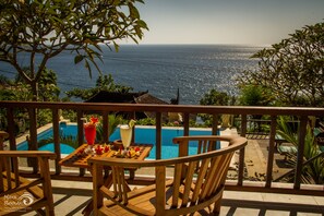 Terraza de madera con mesa y sillas con vista a una piscina y al mar.