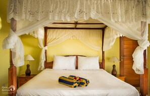 Una cama con dosel y cuatro columnas con ropa blanca, un par de toallas y mesitas de noche de madera con lámparas.