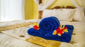 A neatly made bed with a blue towel, a pillow, and a decorative pillow with a floral design. - Beten Waru (Karangasem)