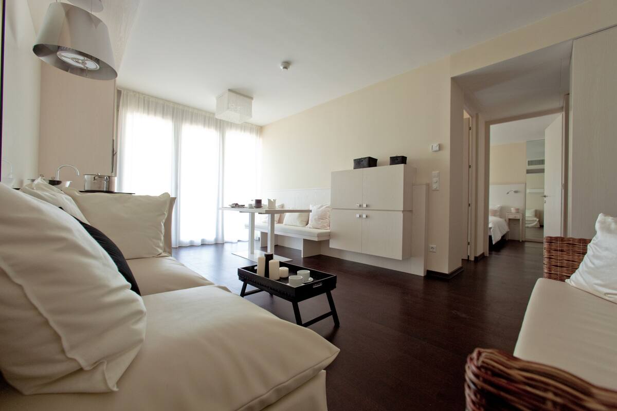 A modern hotel room with a sofa, a small table with candles, a cabinet, and a view of the adjacent bathroom.