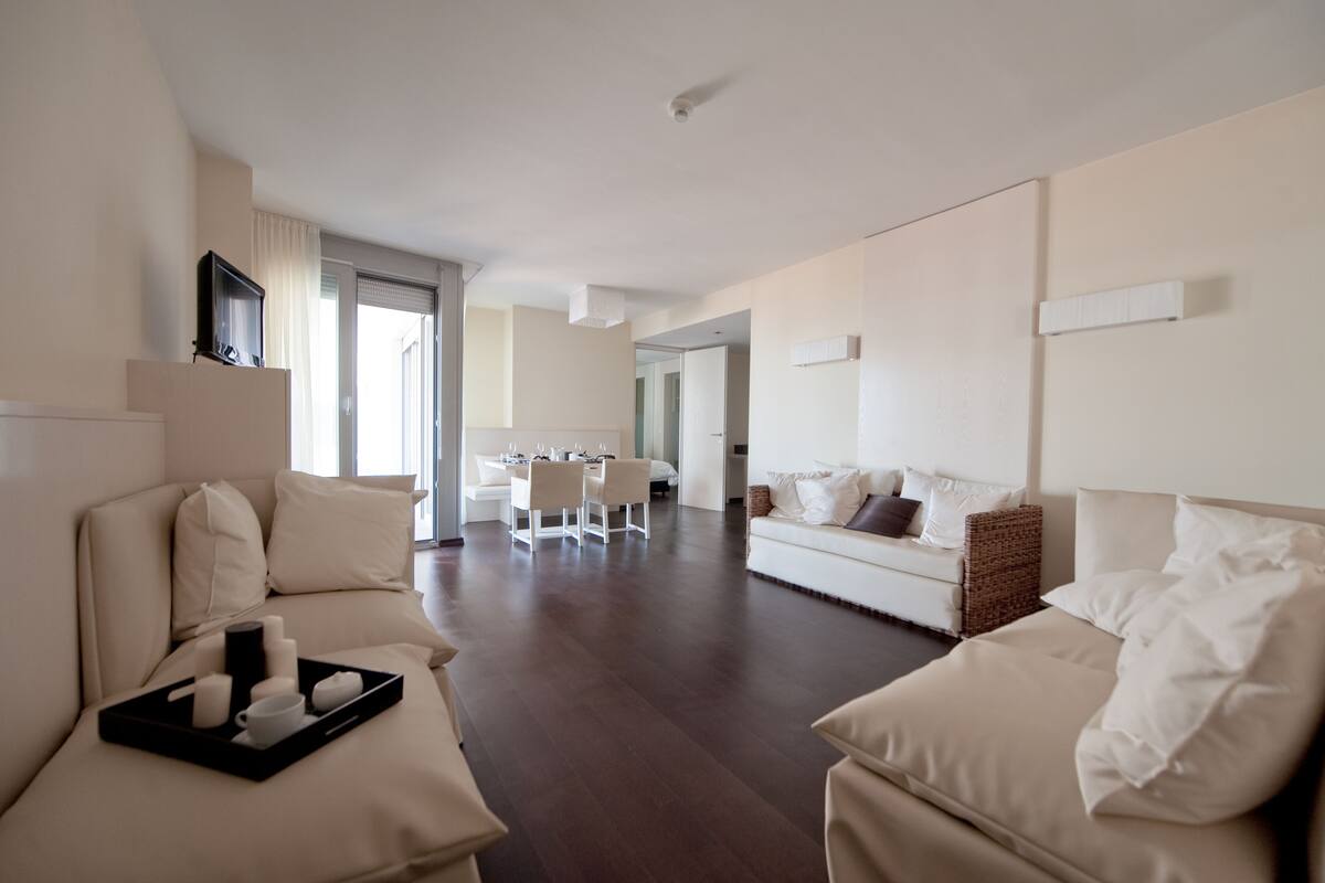 A modern hotel room with a living area, a dining table, and a separate seating area.