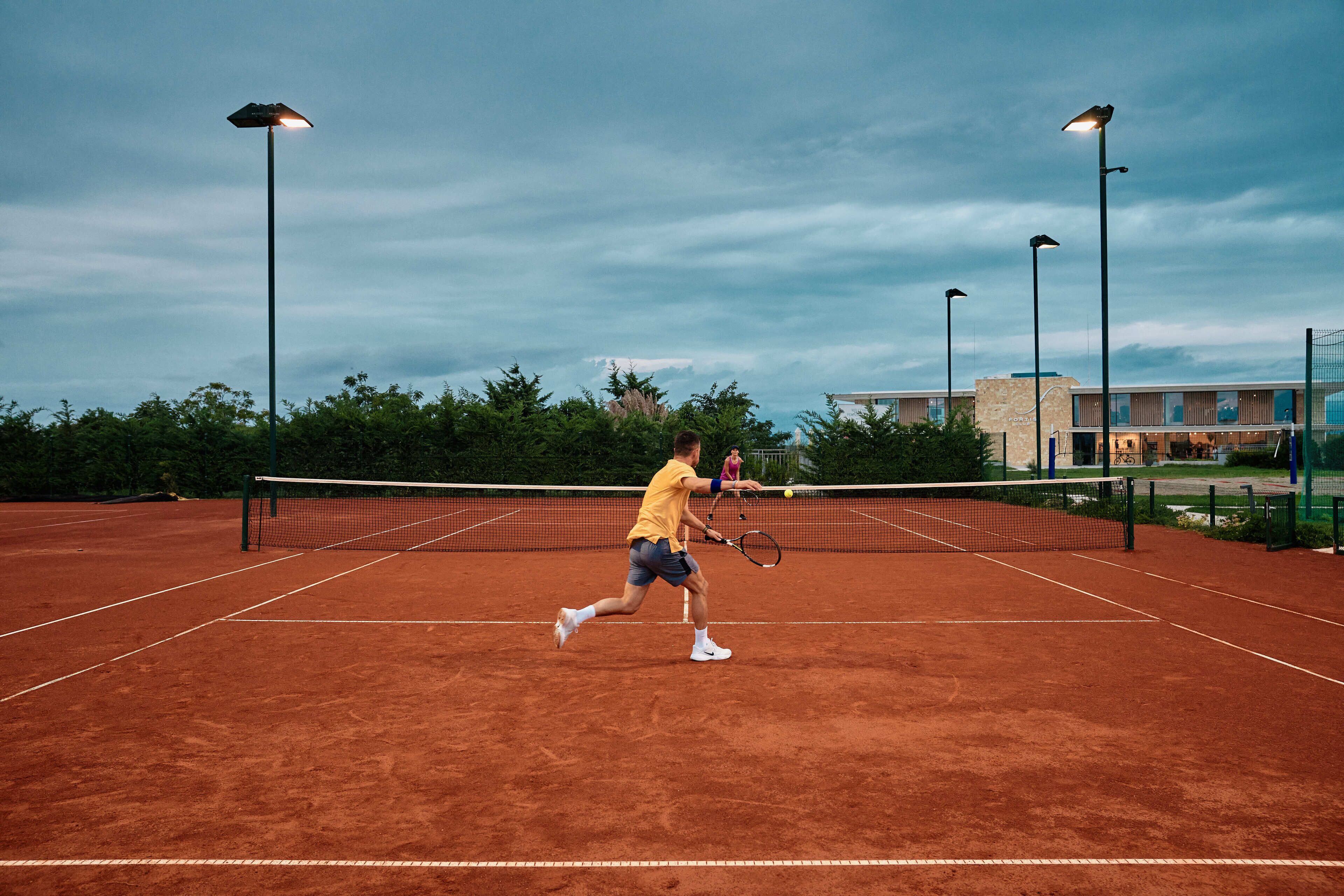 Un court de tennis avec un filet, entouré d’arbres et de bâtiments.