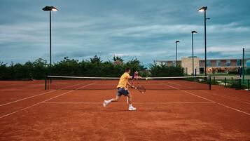 Un court de tennis avec un filet, entouré d’arbres et de bâtiments.