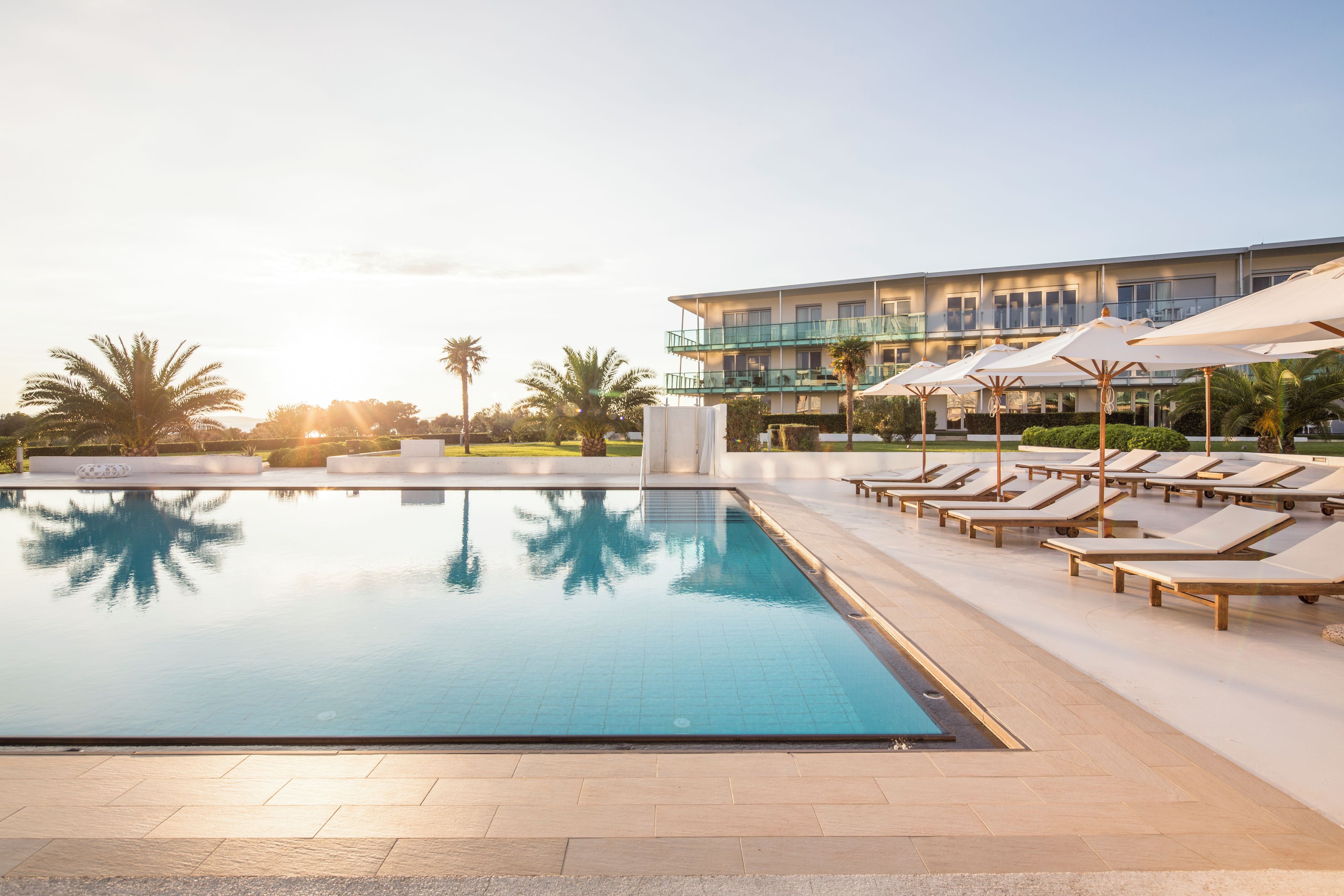 A swimming pool with lounge chairs and umbrellas, surrounded by a building with multiple balconies.