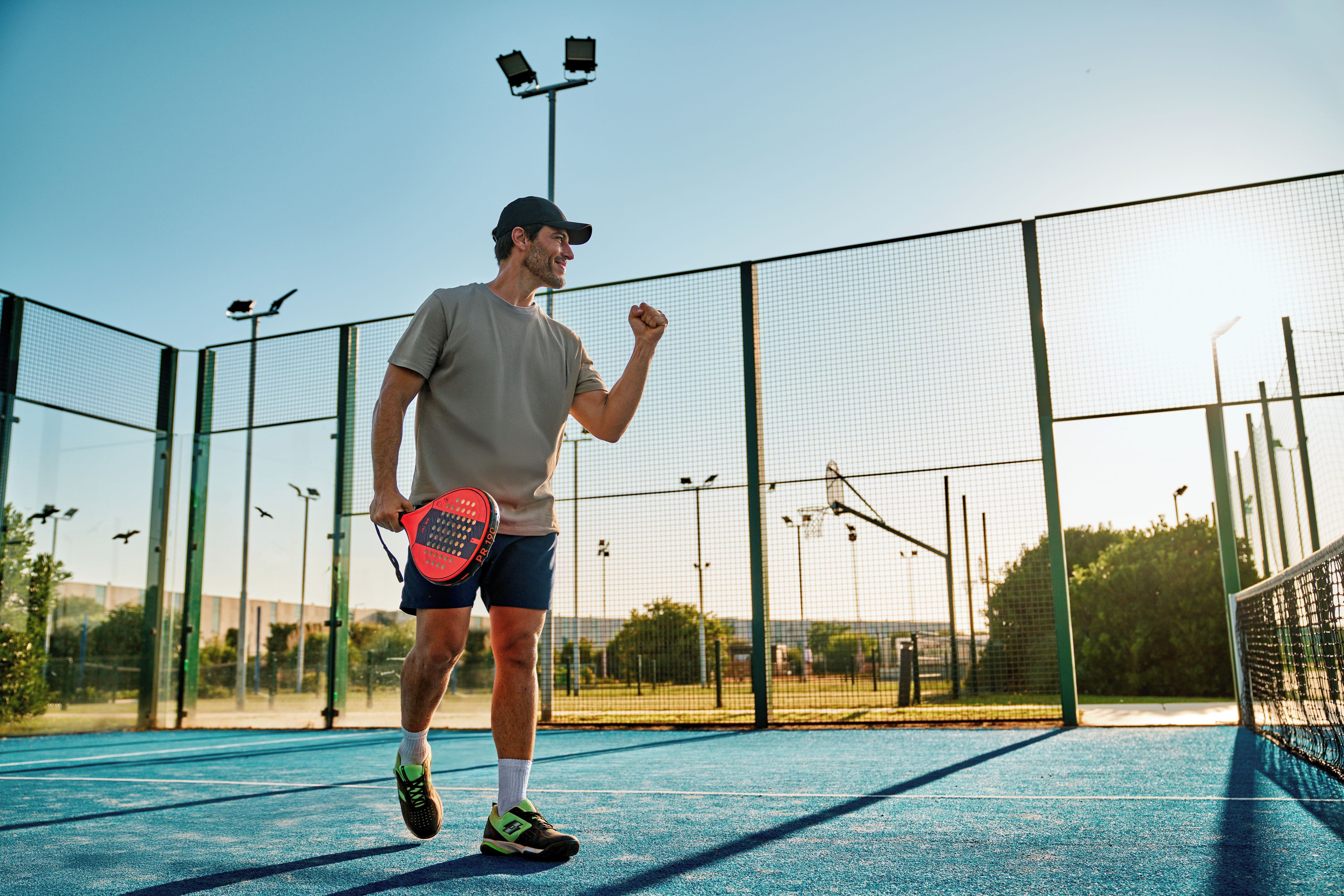 En tennisbana med ett nät, en spelare som håller i ett racket och en klar himmel.