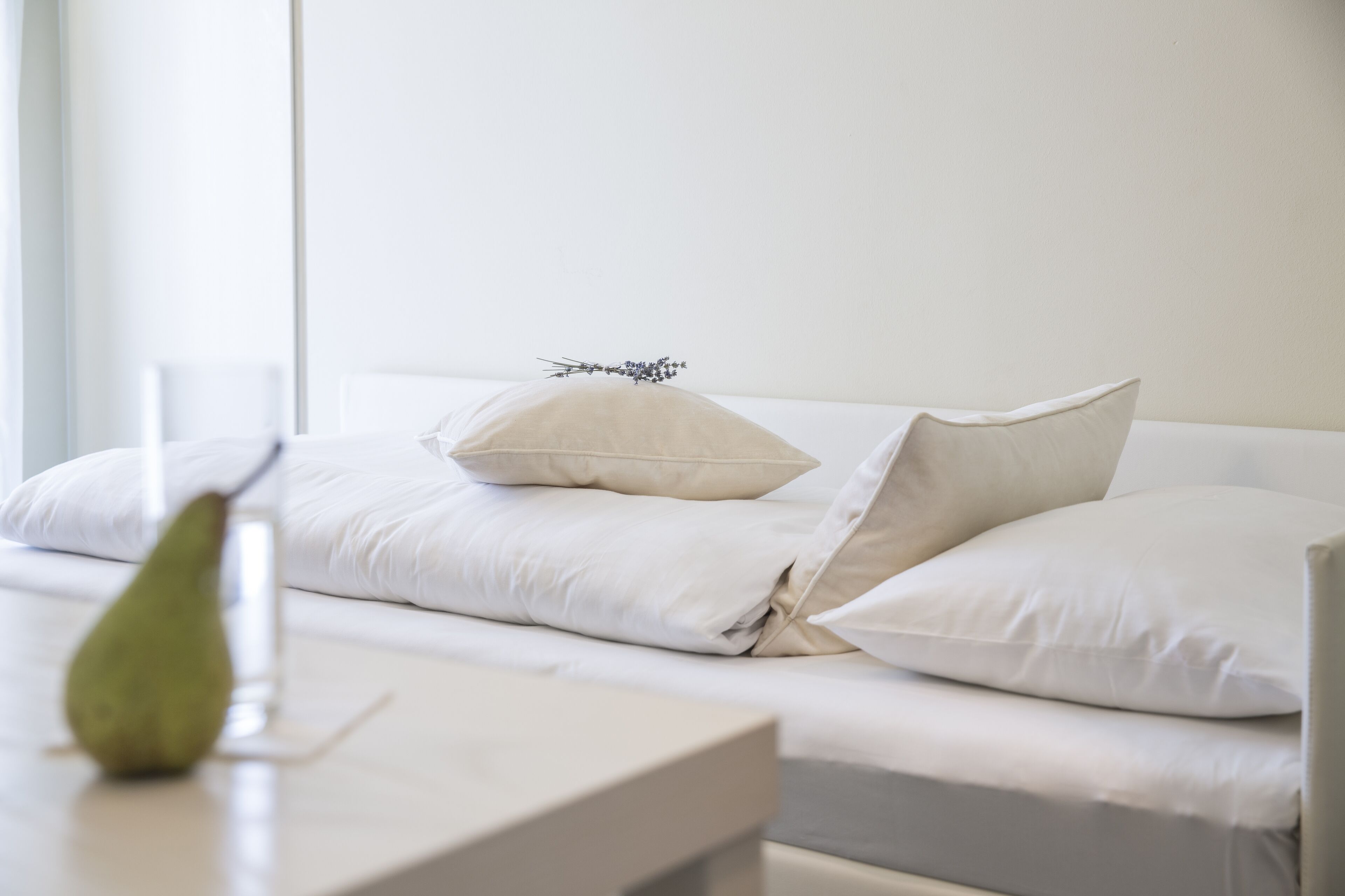 A neatly made bed with white linens and pillows, a bedside table with a green object, and a window with natural light.