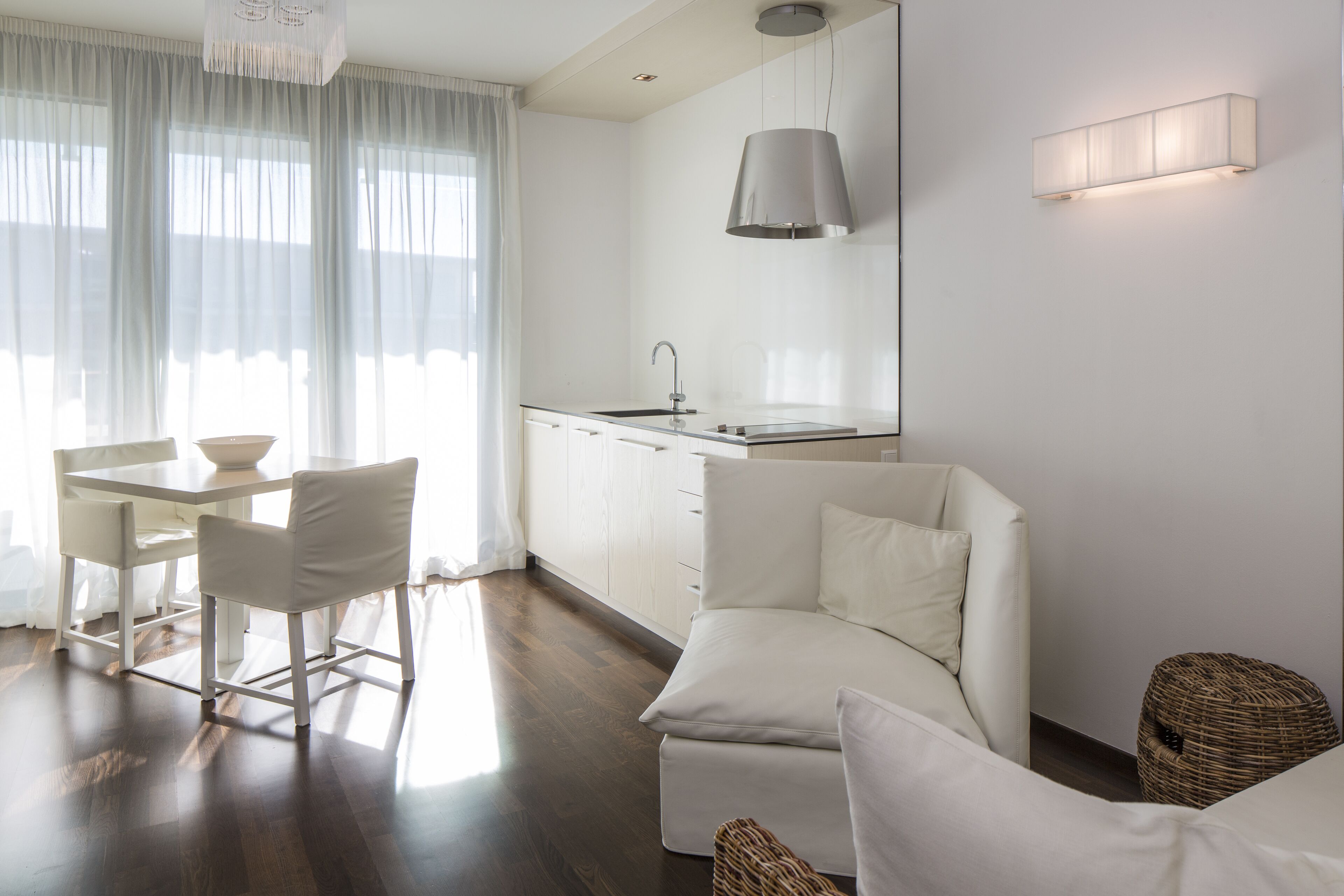 Una sala de estar moderna y minimalista con comedor, cocina y un ventanal con cortinas traslúcidas.