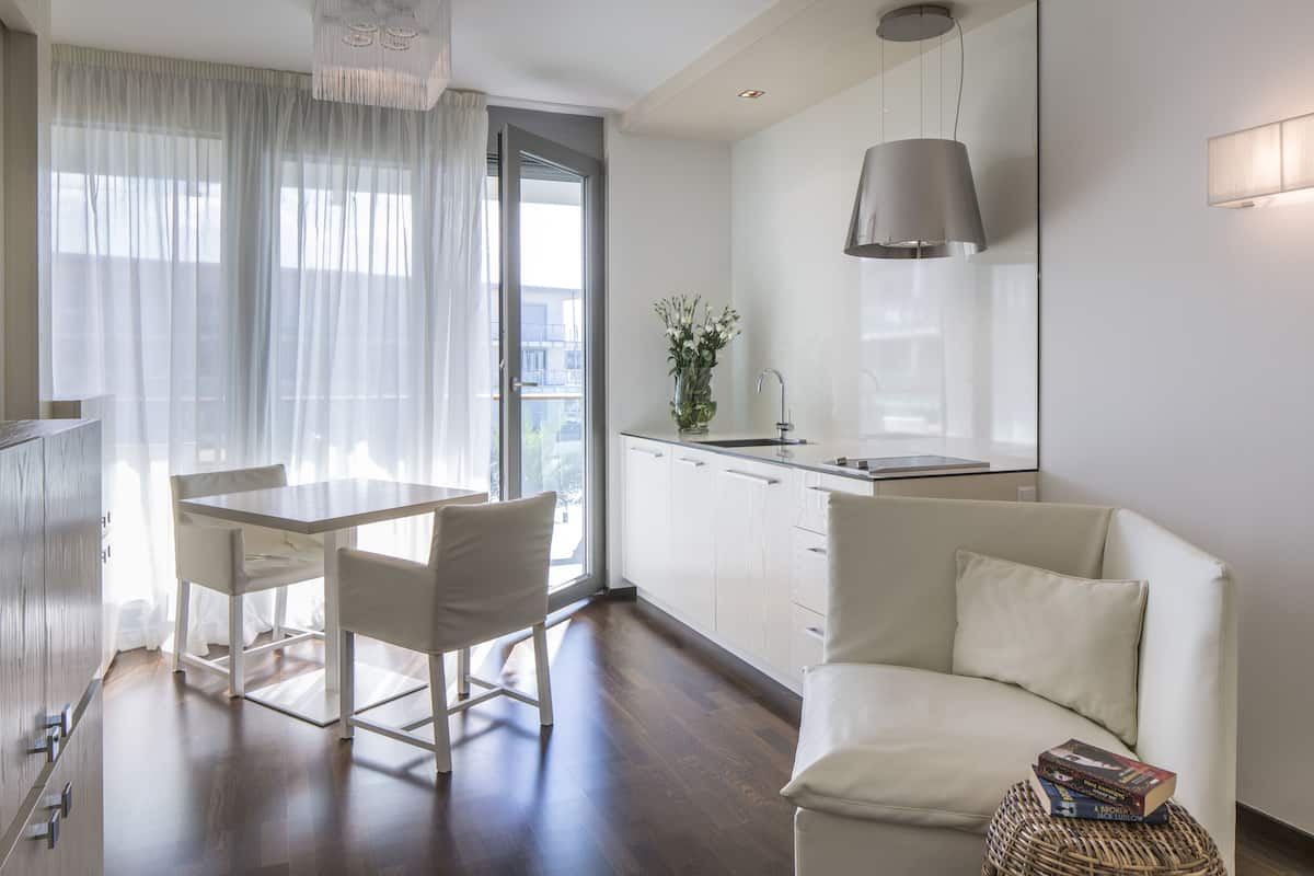A modern kitchen with white cabinets, a dining table with chairs, and a sofa with books.