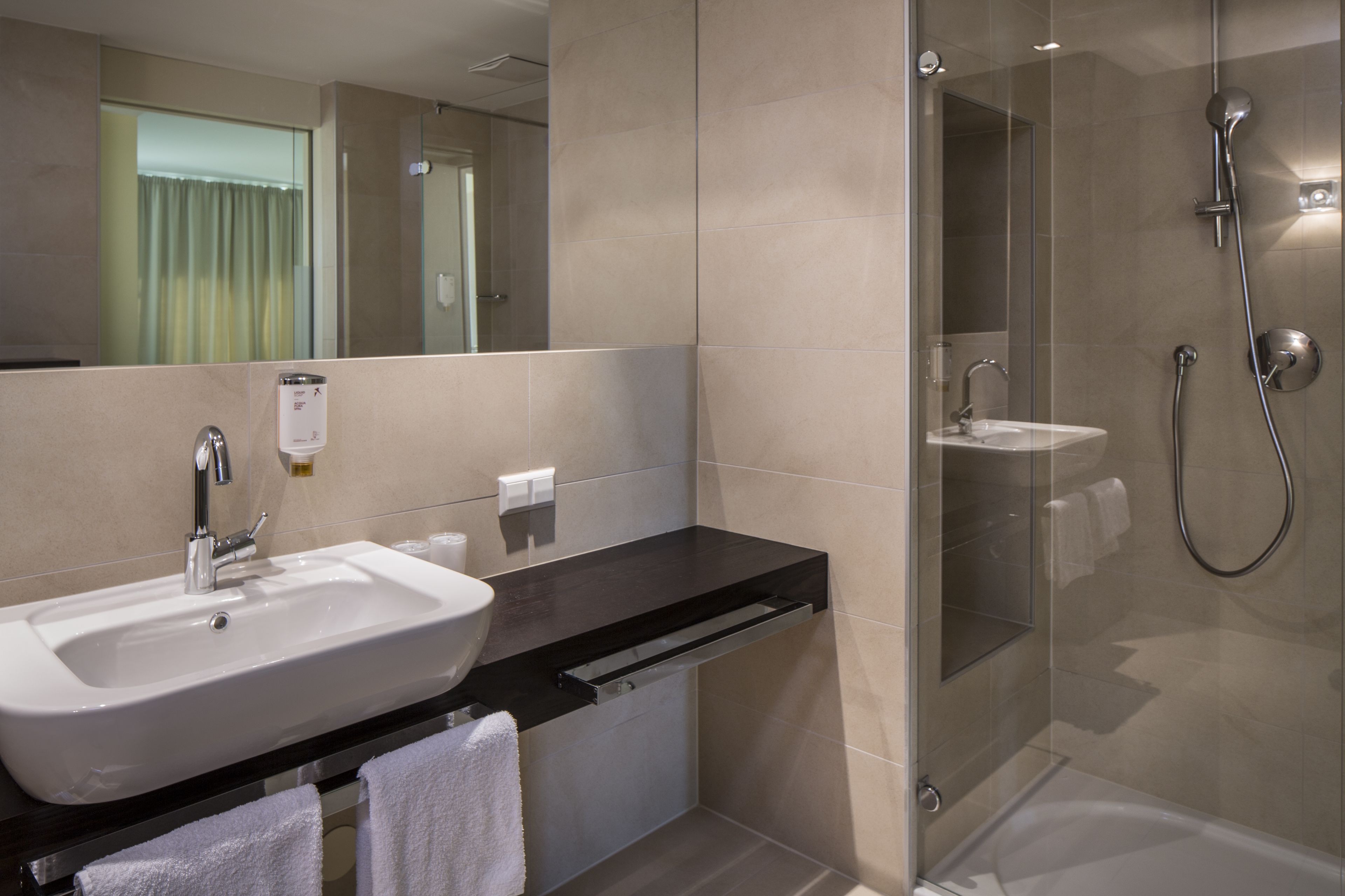Un baño moderno con un lavamanos blanco, un espejo y una zona de ducha con paredes de vidrio.