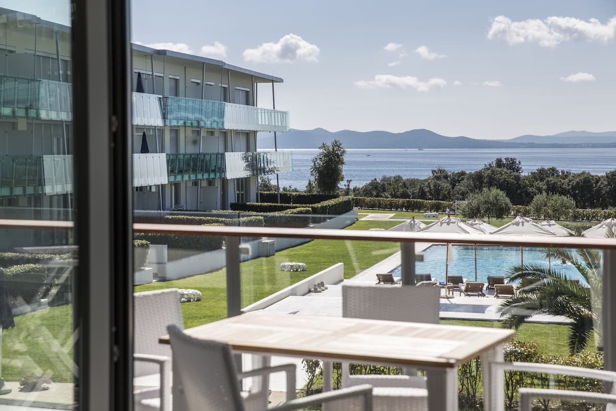 A modern hotel with a pool, outdoor seating, and a view of the sea and mountains.