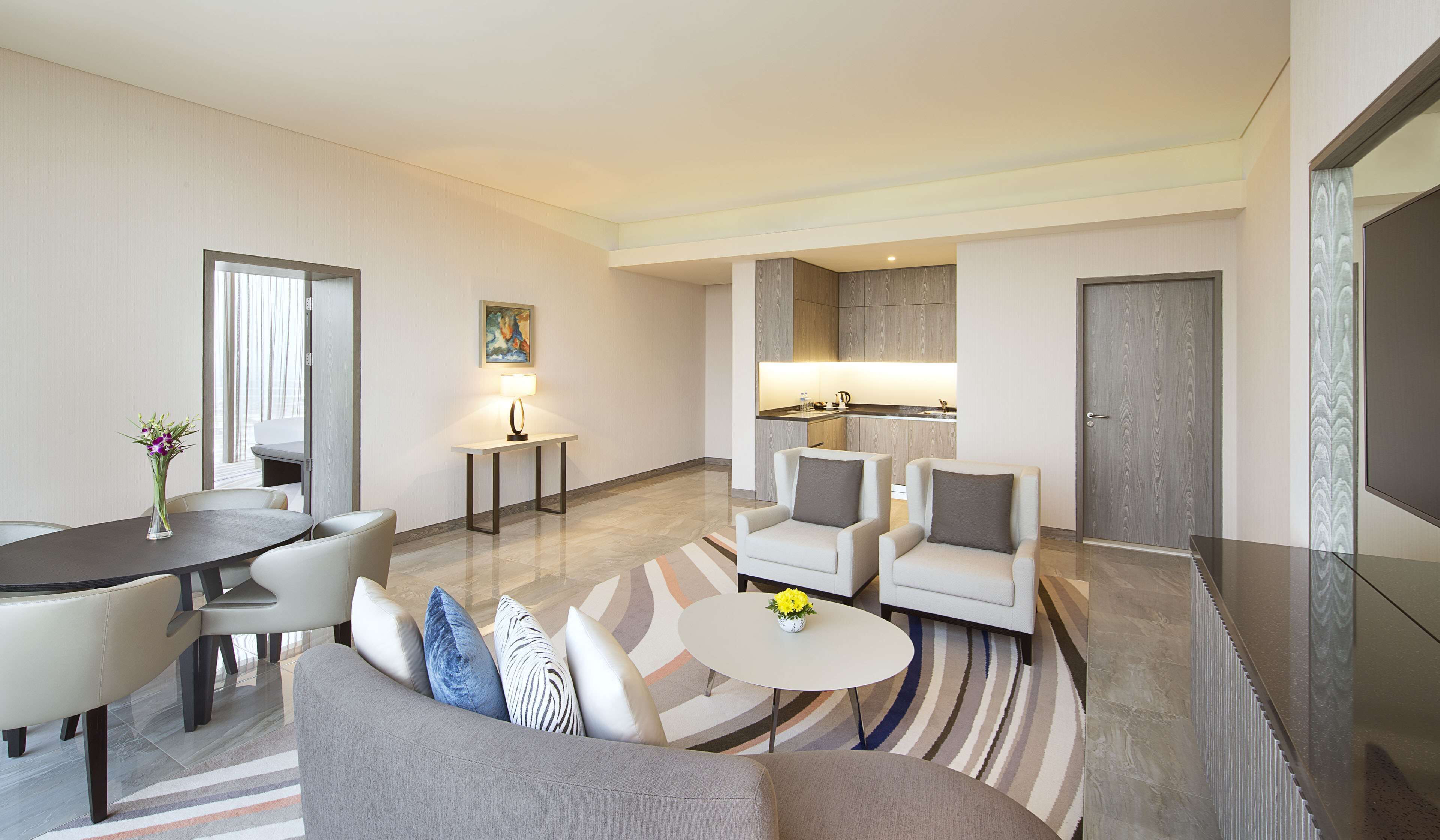Una habitación de hotel moderna con comedor, sofá, una pequeña mesa con flores y una cocina al fondo.
