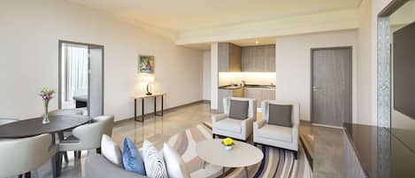 Una habitación de hotel moderna con comedor, sofá, una pequeña mesa con flores y una cocina al fondo.