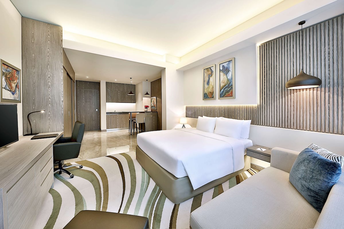 A modern hotel room with a bed, a desk, a chair, a sofa, and a dining area.