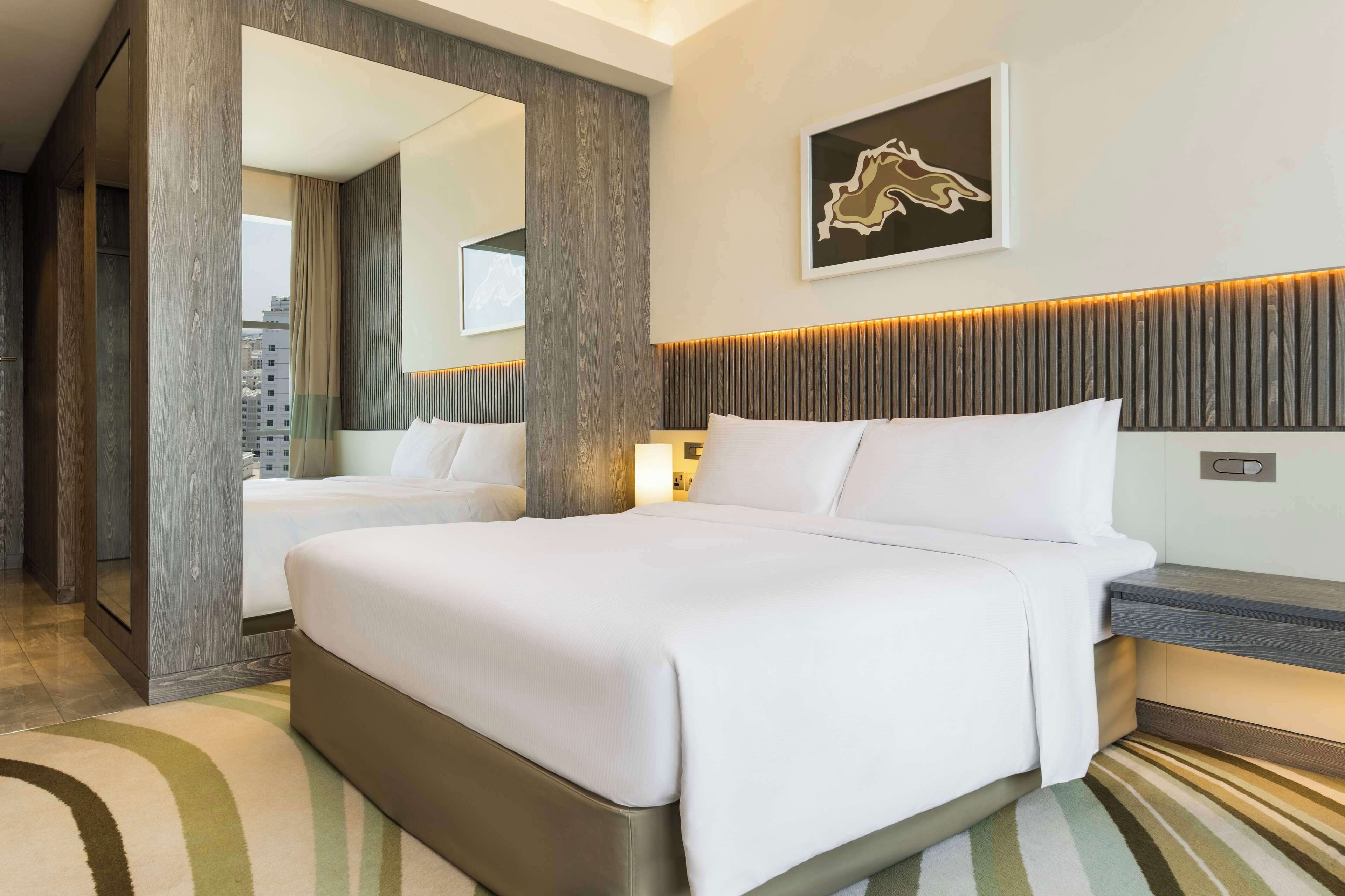 Habitación de hotel moderna con una cama grande, una mesita de noche, un espejo y vistas a la ciudad.
