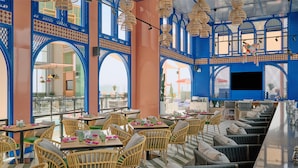A restaurant with wicker furniture, large windows, and blue decorative elements. - DoubleTree by Hilton Hotel Doha Old Town (Doha)