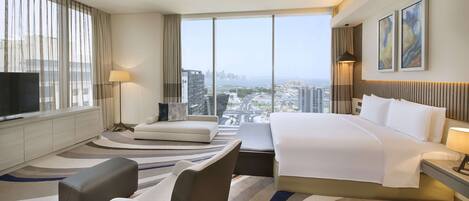 A hotel room with a large bed, a sofa, a TV, and a view of the cityscape.