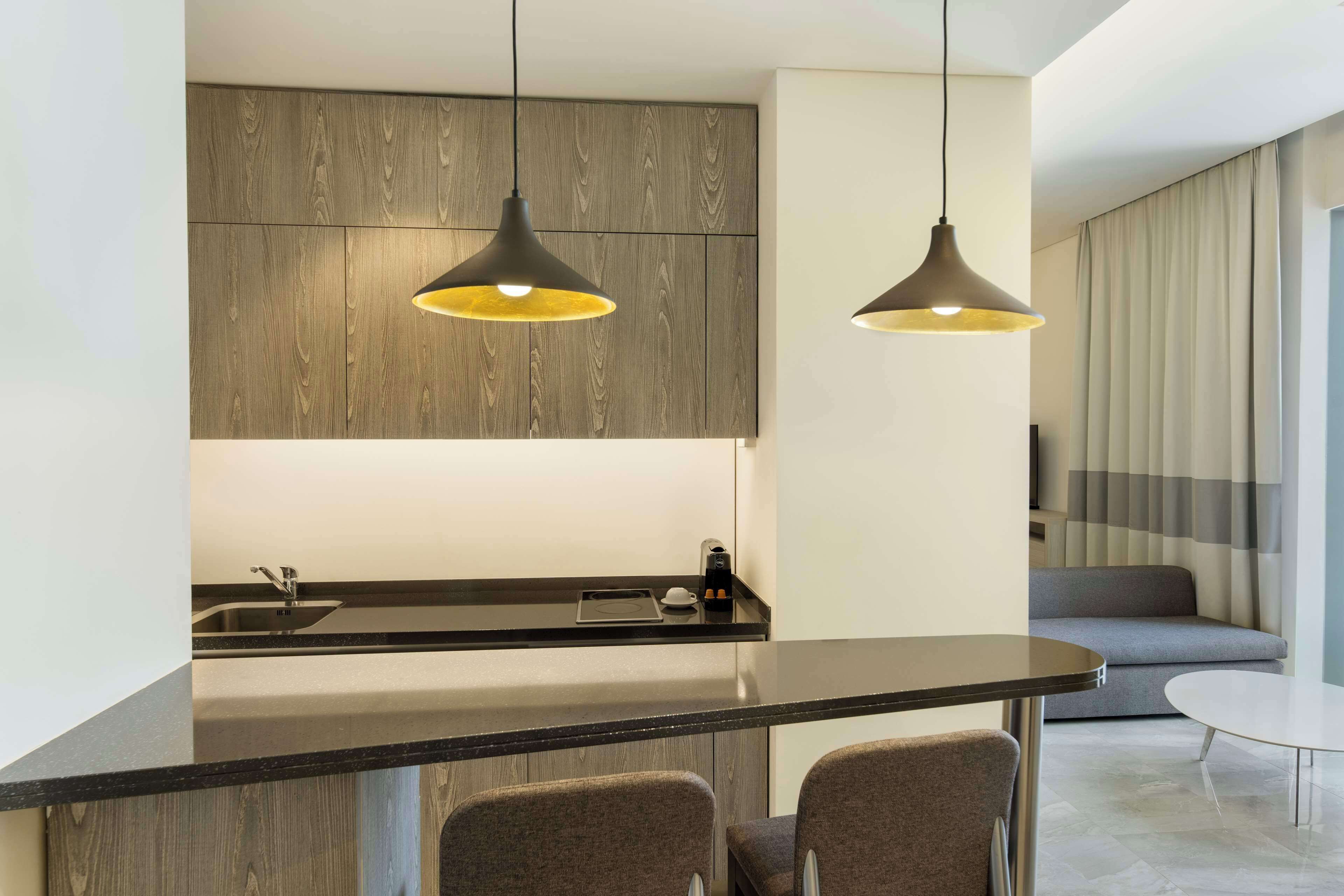 Cozinha moderna com ilha central, luminárias pendentes e área de estar com sofá e mesa.