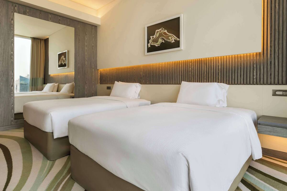 A hotel room with two beds, a large mirror, and a city view.