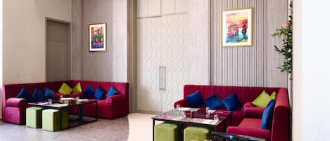 Un moderno vestíbulo de hotel con sofás rojos, otomanas verdes y una mesa de centro de madera.