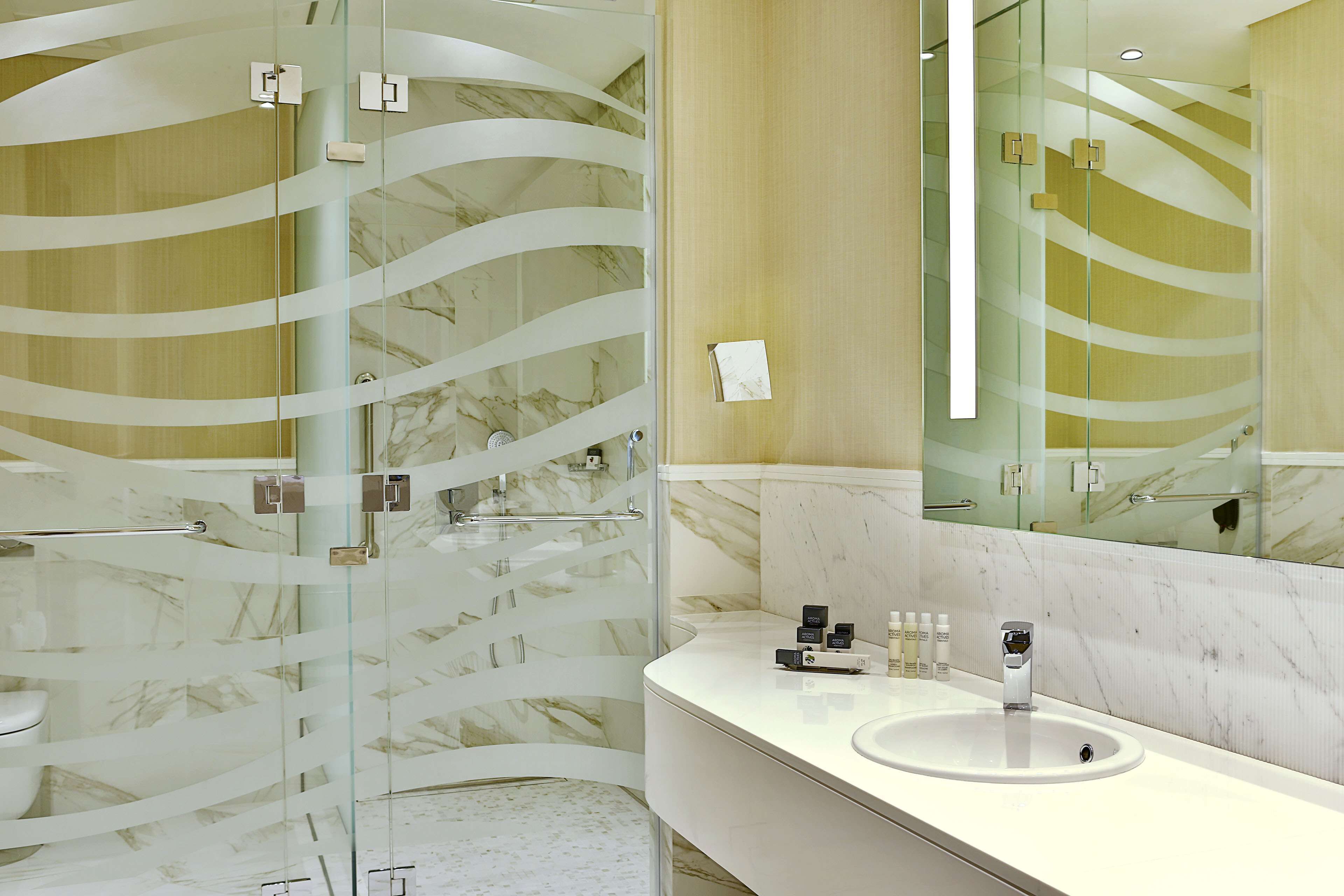 Ein modernes Badezimmer mit einer Duschkabine aus Glas, einer Wand mit Marmorplatten und einem großen Spiegel über dem Waschbecken.