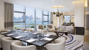 A modern hotel room with a large dining table, comfortable seating, a sofa, and a view of a city skyline and water. - DoubleTree by Hilton Hotel Doha Old Town (Doha)
