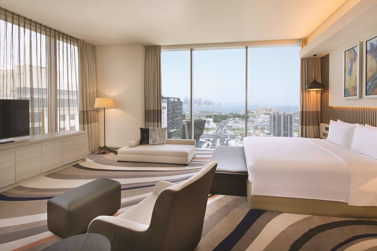 A hotel room with a large bed, a sofa, a TV, and a view of the cityscape.