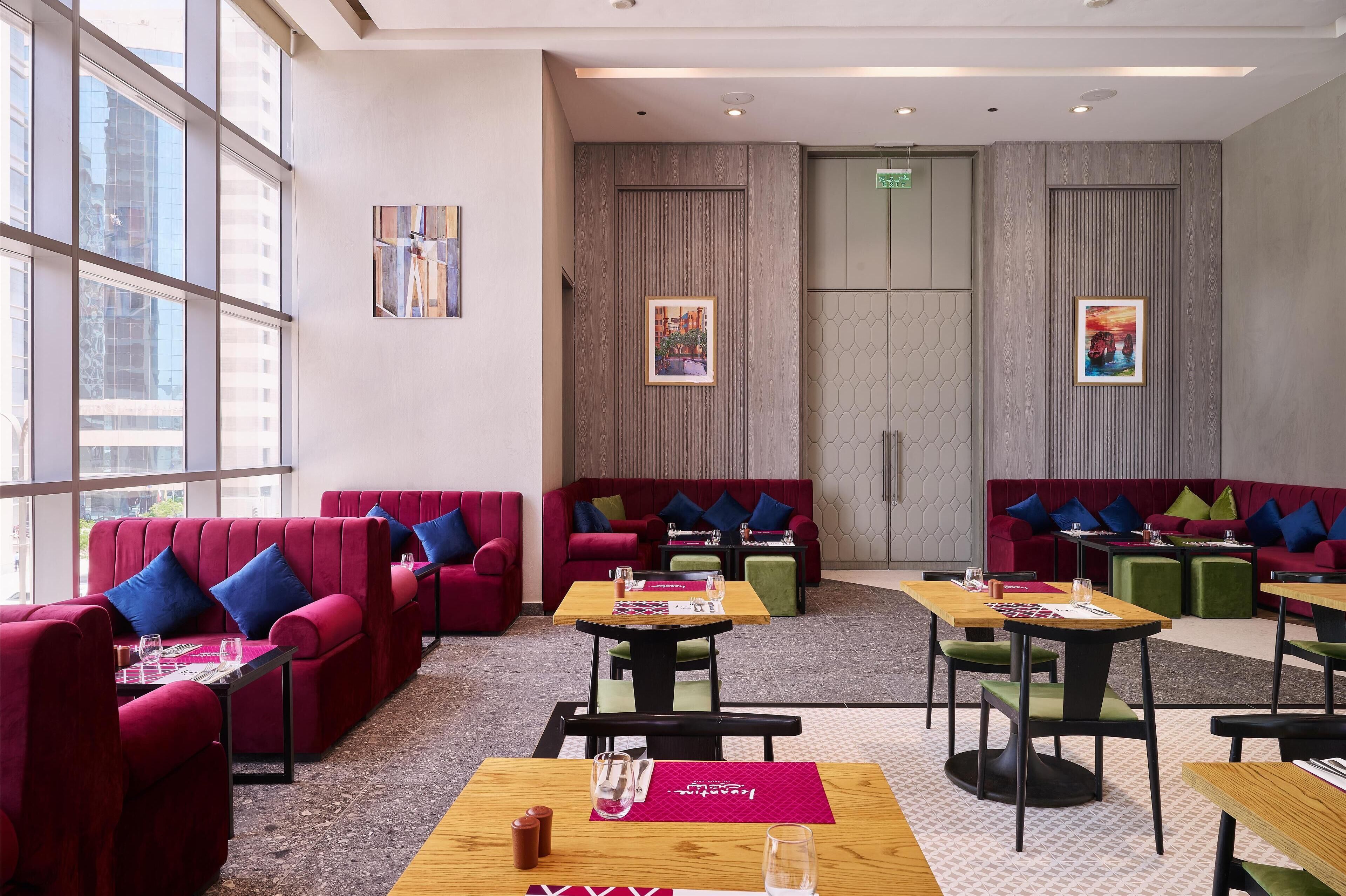 A modern lounge area with red sofas, green and blue cushions, and wooden tables.