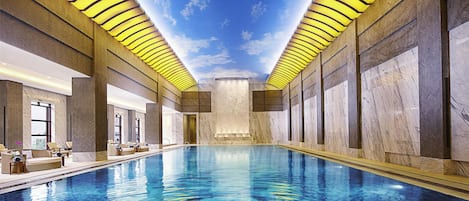 Ein Innenpool mit einer Decke, die Himmel und Wolken simuliert, umgeben von Wänden mit Zickzackmuster und Marmor.