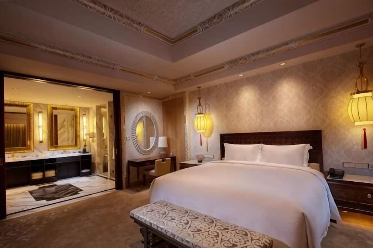 A spacious bedroom with a large bed, a sitting bench, a vanity with a mirror, and two wall-mounted lamps.