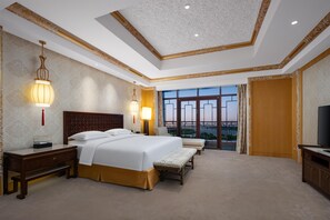A hotel room with a large bed, bedside tables, a TV, and a balcony with a city view.