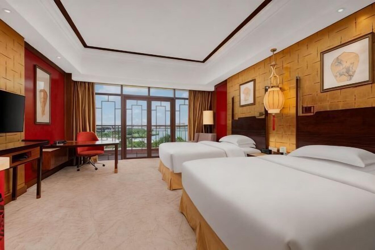 Een hotelkamer met een groot raam, een bureau, een stoel, twee bedden en een televisie.