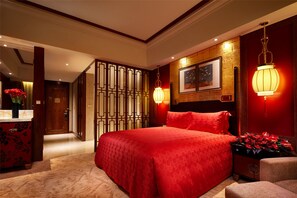 Quarto de hotel com uma cama grande, cabeceira de madeira, painel decorativo na parede, quadro emoldurado e mesa de cabeceira com flores.
