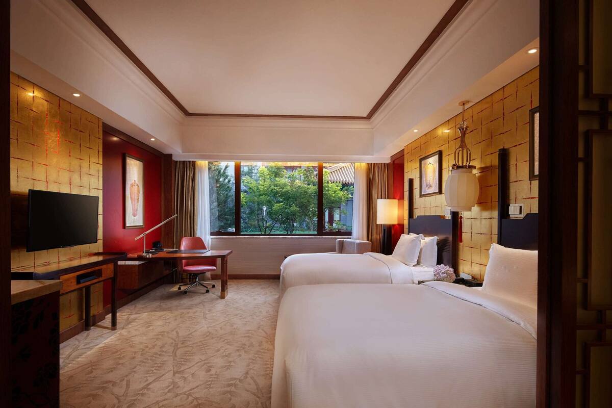 Une chambre d’hôtel avec un grand lit, un bureau avec une chaise, une télévision et une fenêtre donnant sur un paysage verdoyant.