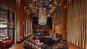 Een moderne hotel lobby met een bar in het midden, zitmogelijkheden en een decoratieve kroonluchter.