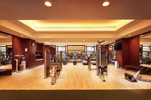 Une salle de sport spacieuse, dotée de divers appareils d’exercice, d’un plancher en bois et de grandes fenêtres laissant entrer la lumière naturelle.
