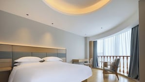 A modern hotel room with a large bed, a desk, and a balcony with curtains. - Baigang International Hotel (Chengdu)