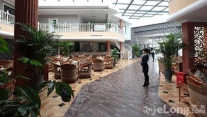 A spacious indoor area with a high ceiling, a central staircase, and multiple seating areas with wicker furniture. - Baigang International Hotel (Chengdu)