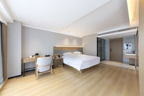 A modern hotel room with a bed, a desk, a chair, and a bathroom visible through an open door. - Baigang International Hotel (Chengdu)