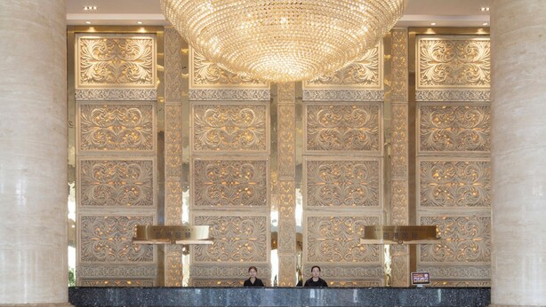 A lobby with ornate wall panels, a grand chandelier, and a reception desk. - Baigang International Hotel (Chengdu)