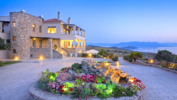 A modern house with a stone facade, a balcony, and a landscaped garden with flowers and rocks. -  Villa Marini (Aegina)
