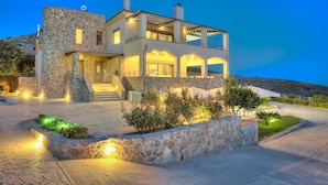 A modern two-story stone house with a balcony, a stone entrance, and a landscaped garden area. -  Villa Marini (Aegina)