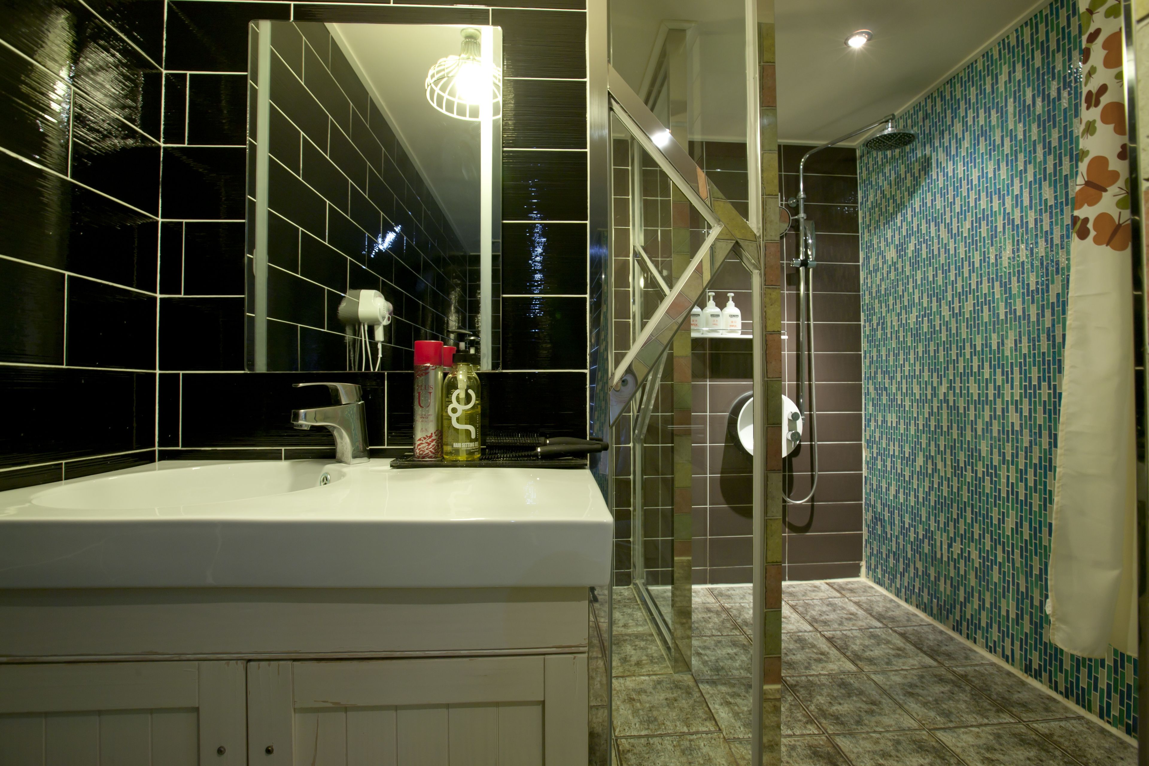 Un baño con un lavamanos blanco, una mampara de ducha de vidrio y una pared con azulejos de diseño azul.