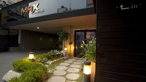 L’extérieur du Max Motel présente un chemin en pierre menant à l’entrée, bordé de verdure et éclairé par des lampes fixées aux murs.